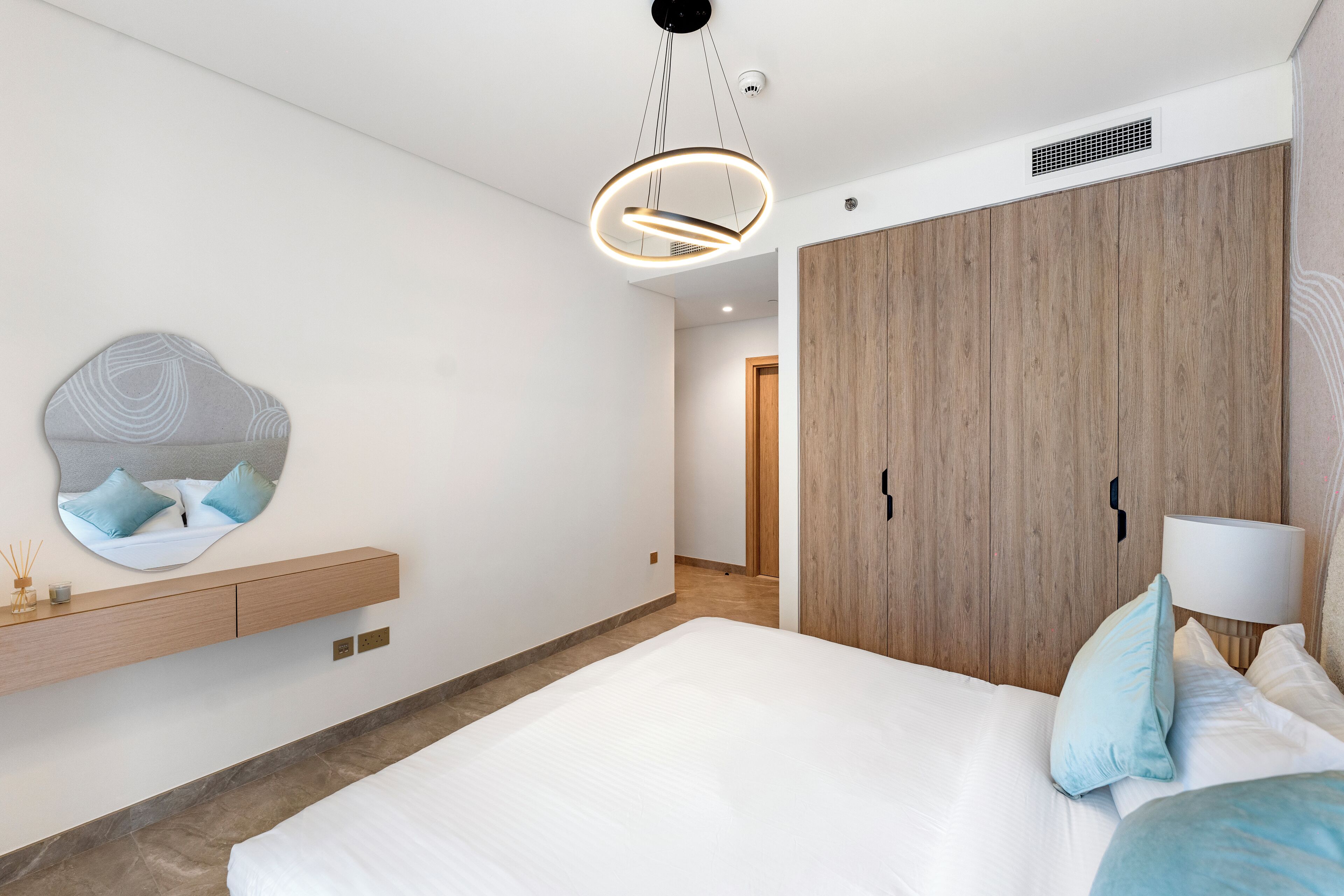 A modern bedroom with a large bed, a wooden wardrobe, a built-in shelf, and a unique circular light fixture.