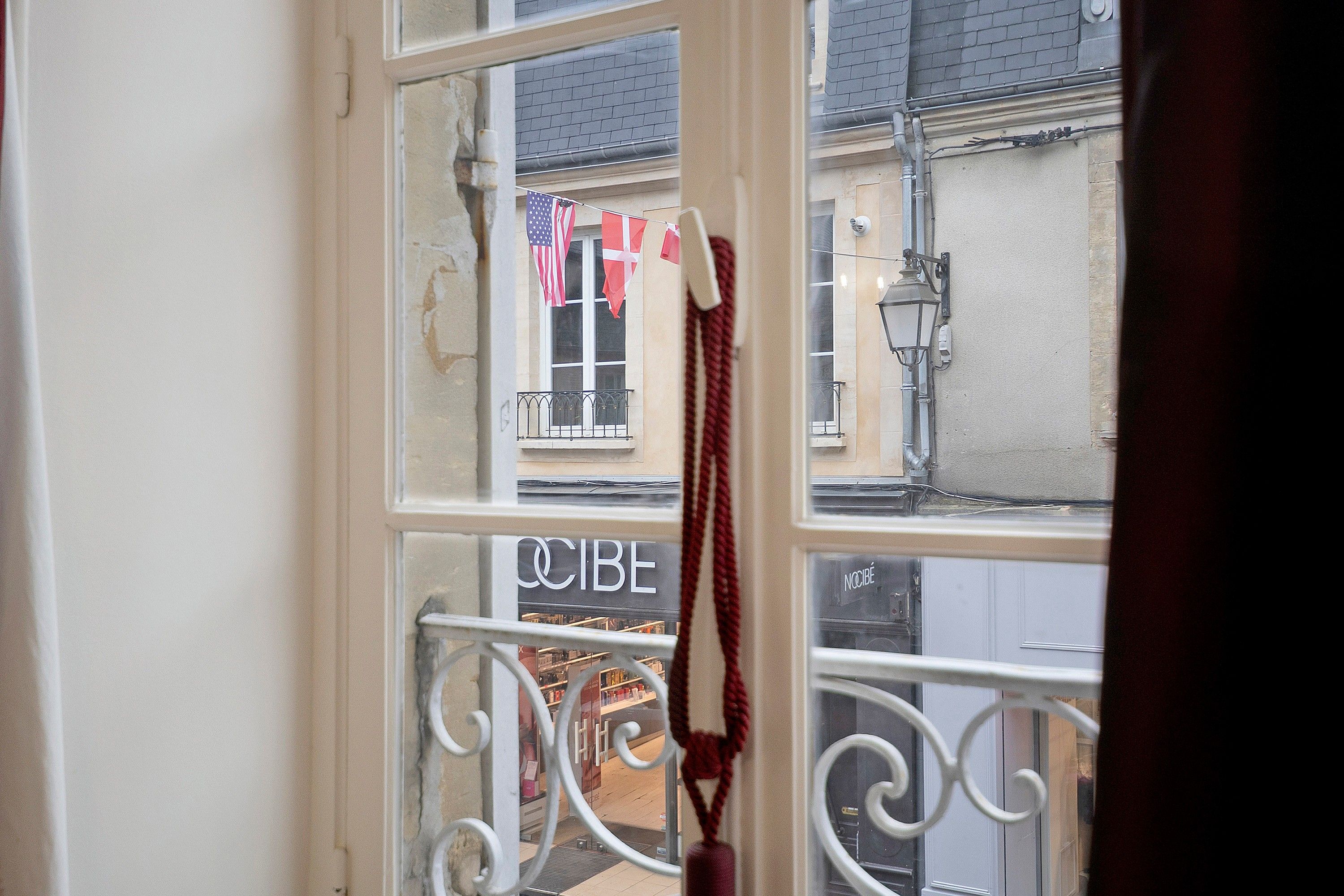 Une vue à travers une fenêtre ornée d’une rambarde en métal, avec un drapeau et une enseigne sur laquelle on peut lire « CIBE ».