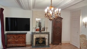 A room with a television, a chandelier, a wooden cabinet, a fireplace, and a door.