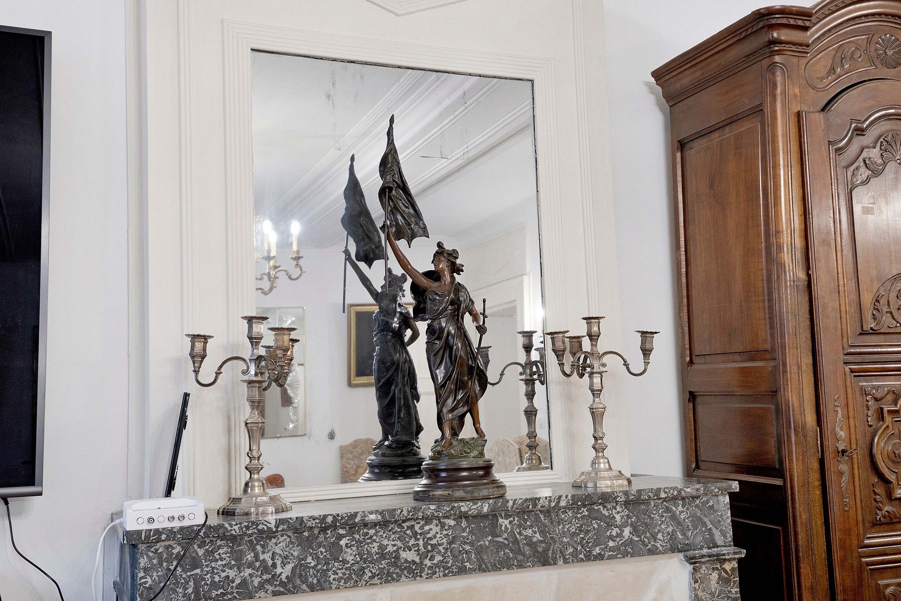 Una chimenea de mármol con una estatua, candelabros y un aparador de madera.