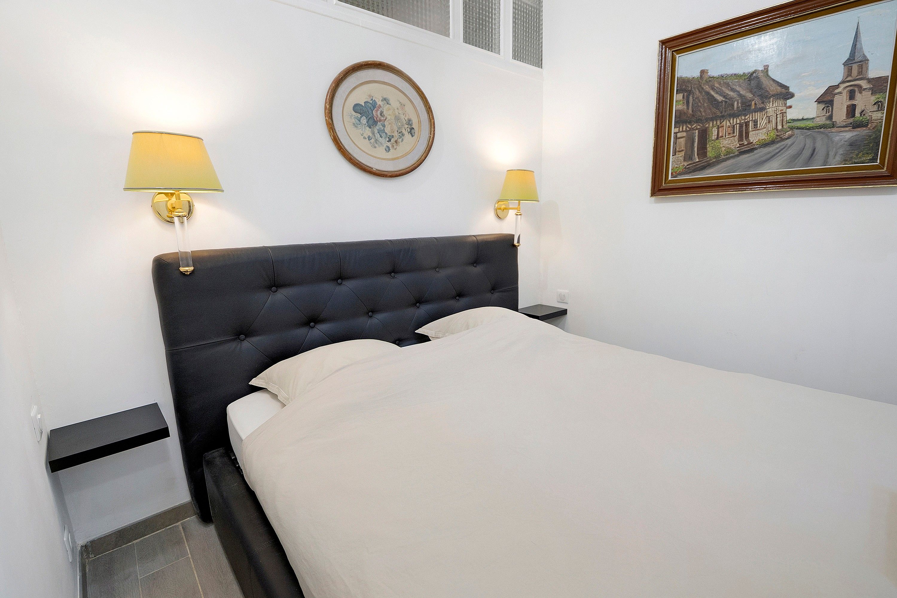 Une chambre d’hôtel avec un lit, deux lampes de chevet, un tableau encadré au mur et une petite poubelle.