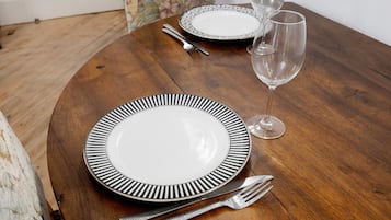 Een ronde houten tafel met een wit bord met een zwarte rand, een vork, een mes en een wijnglas.