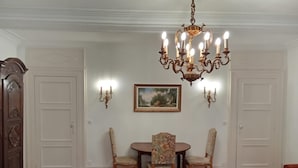 A dining area with a chandelier, two chairs, a table, and a painting on the wall.