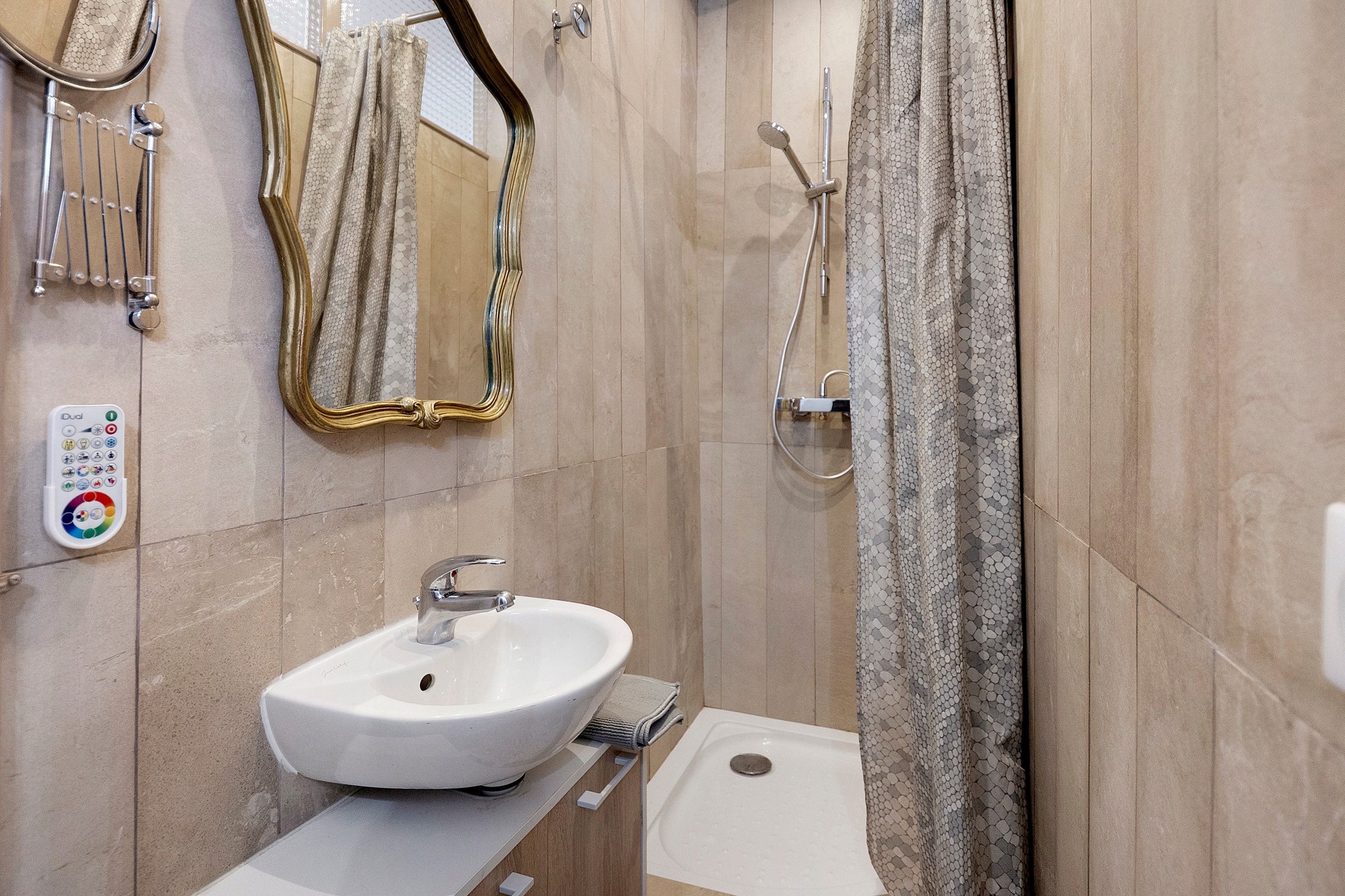 Een badkamer met een witte wastafel, een handdouche, een spiegel met gouden lijst en een bedieningspaneel met een kleurenwiel.