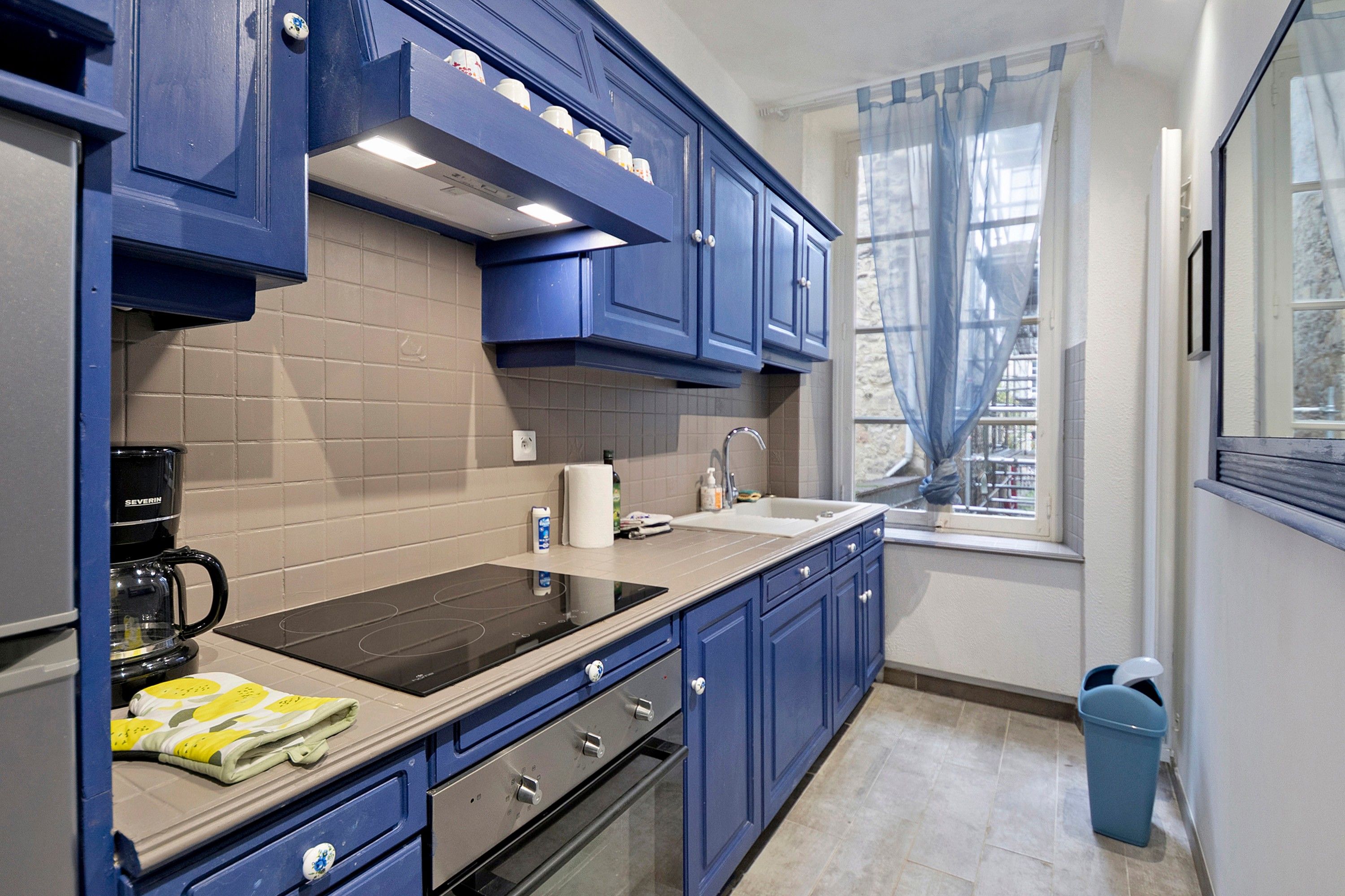 A modern kitchen with blue cabinets, a black stove, and a window with sheer curtains.