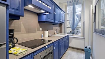 A modern kitchen with blue cabinets, a black stove, and a window with sheer curtains.