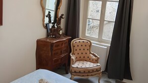 A bedroom with a bed, a wooden dresser, a chair, a mirror, and a window with curtains.