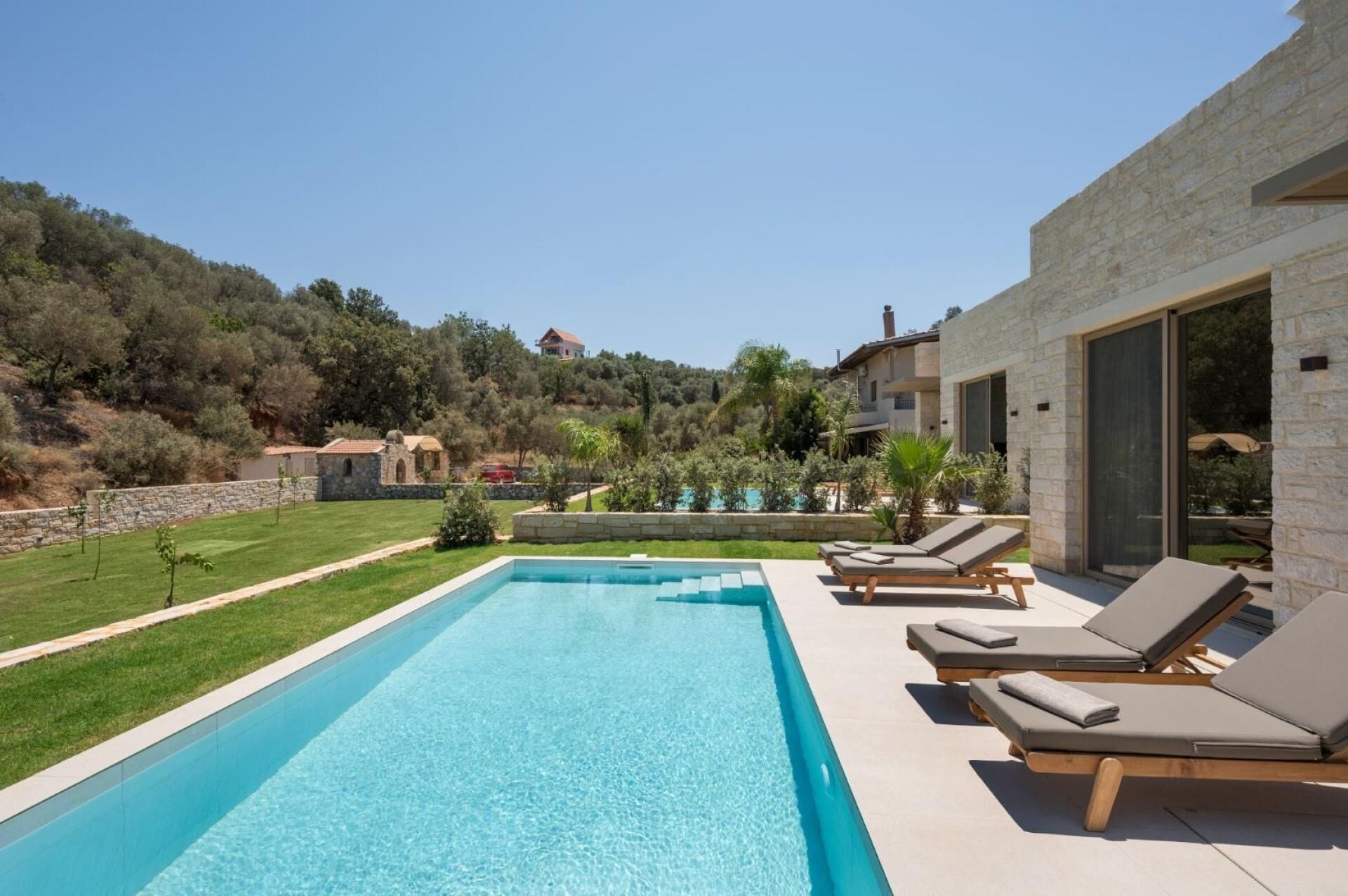 Une piscine avec des chaises longues, un bâtiment en pierre et une vue sur une colline, avec des arbres et une maison au loin.