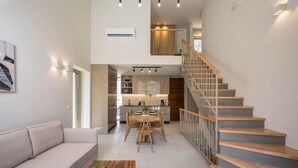 A modern living room with a sofa, a coffee table with a plant, and a staircase leading to a kitchen area. - La Divina Villa (Zoe) (Chania)