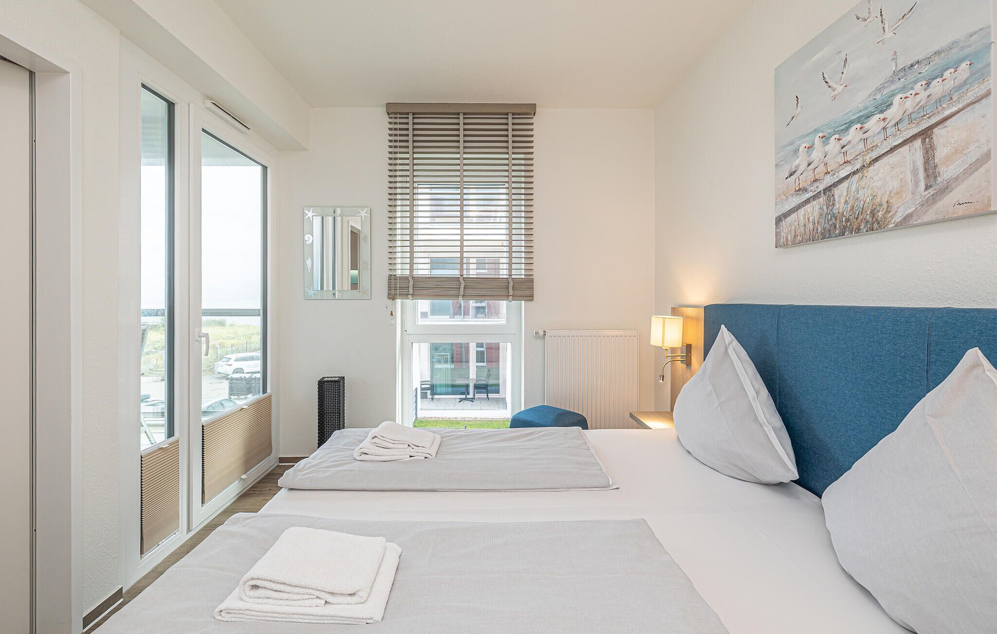 A hotel room with a large bed, a window with blinds, a view of the outside, and a painting on the wall.