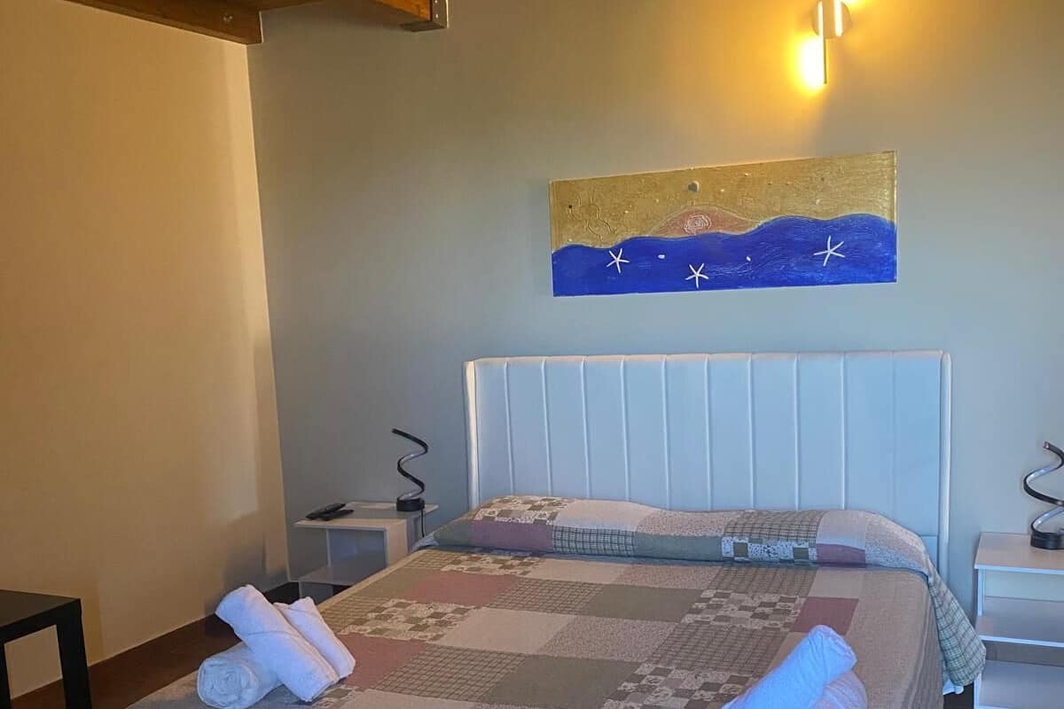 Una cama bien hecha con colcha y toallas enrolladas, una obra de arte en la pared y techo de madera.