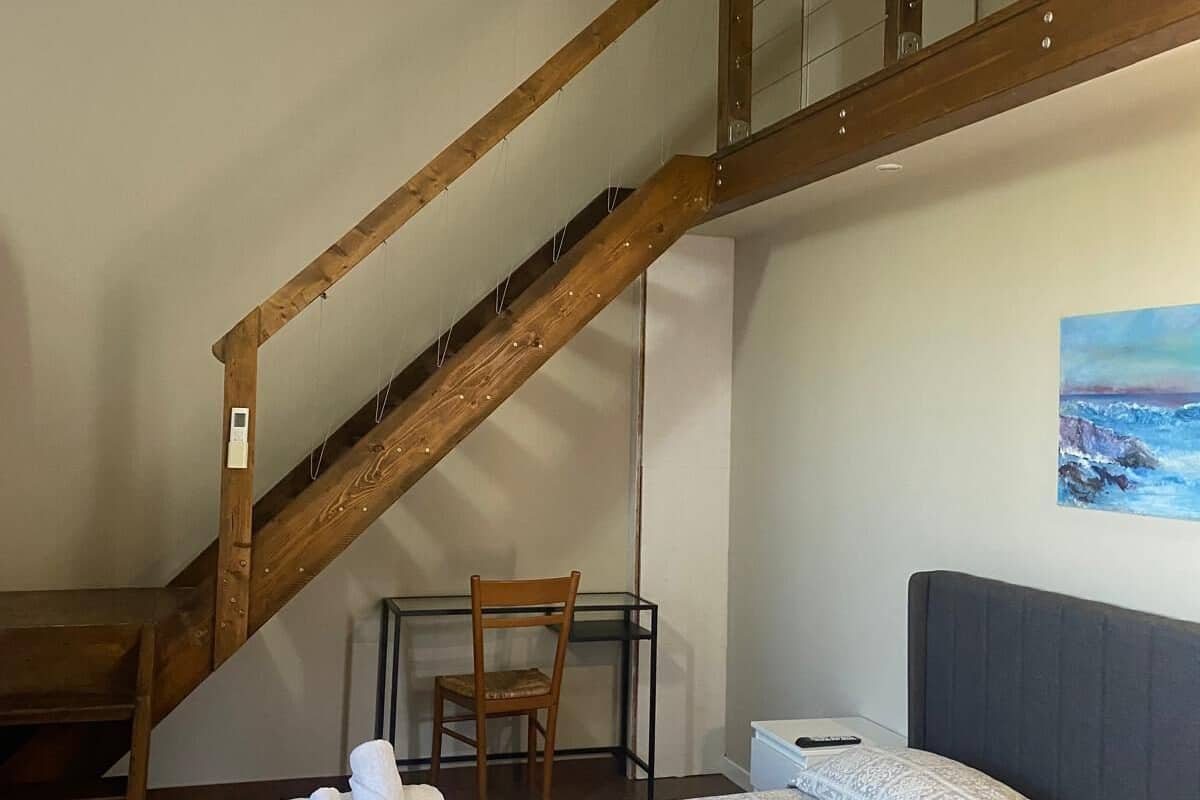Una habitación de hotel con una cama, una silla, un cuadro en la pared y una escalera de madera.