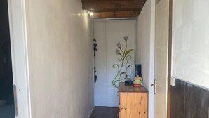 A narrow hallway with wooden ceiling beams, a wooden cabinet with a kettle, and a door with a floral design. - Stone House Gebel el Son (Novi Velia)
