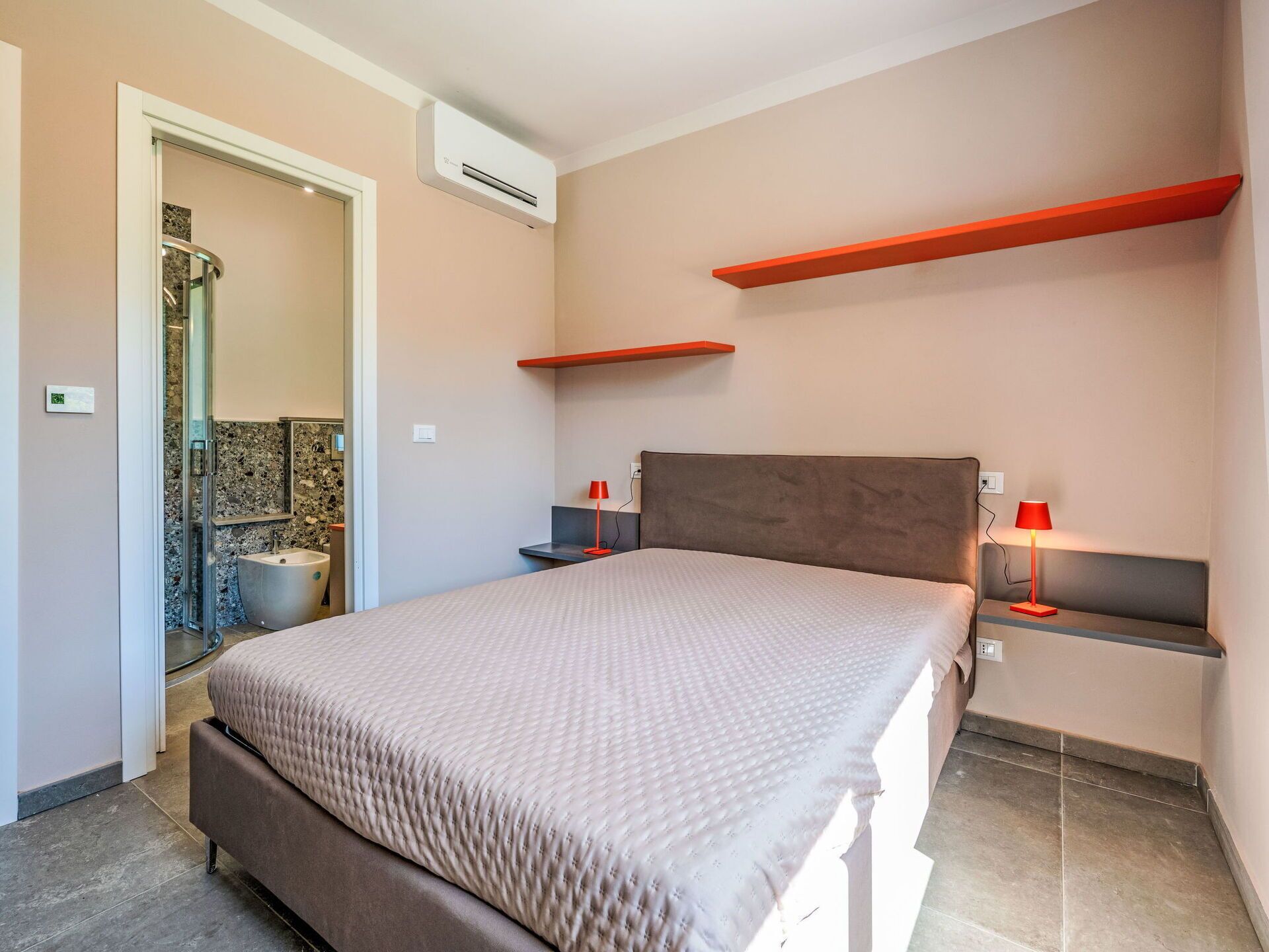 Une chambre moderne équipée d’un lit, de lampes de chevet, d’une douche et d’un système de climatisation intégré.