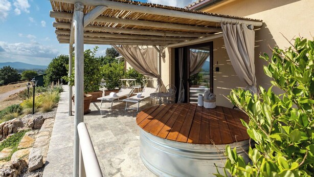 Ein überdachter Außenbereich mit Holzterrasse, Liegestühlen und Whirlpool.