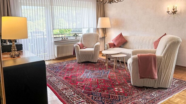Een moderne woonkamer met een bank, twee fauteuils, een salontafel en een kamerbreed tapijt.