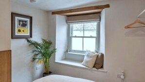 Un dormitorio con cama, ventana con vistas, planta y cuadro en la pared.