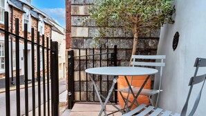 Un pequeño espacio exterior con mesa y sillas de metal, una planta en maceta y un muro de piedra.