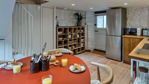Una cocina moderna con comedor, que incluye una mesa redonda con utensilios para el desayuno, una estantería empotrada y un refrigerador.