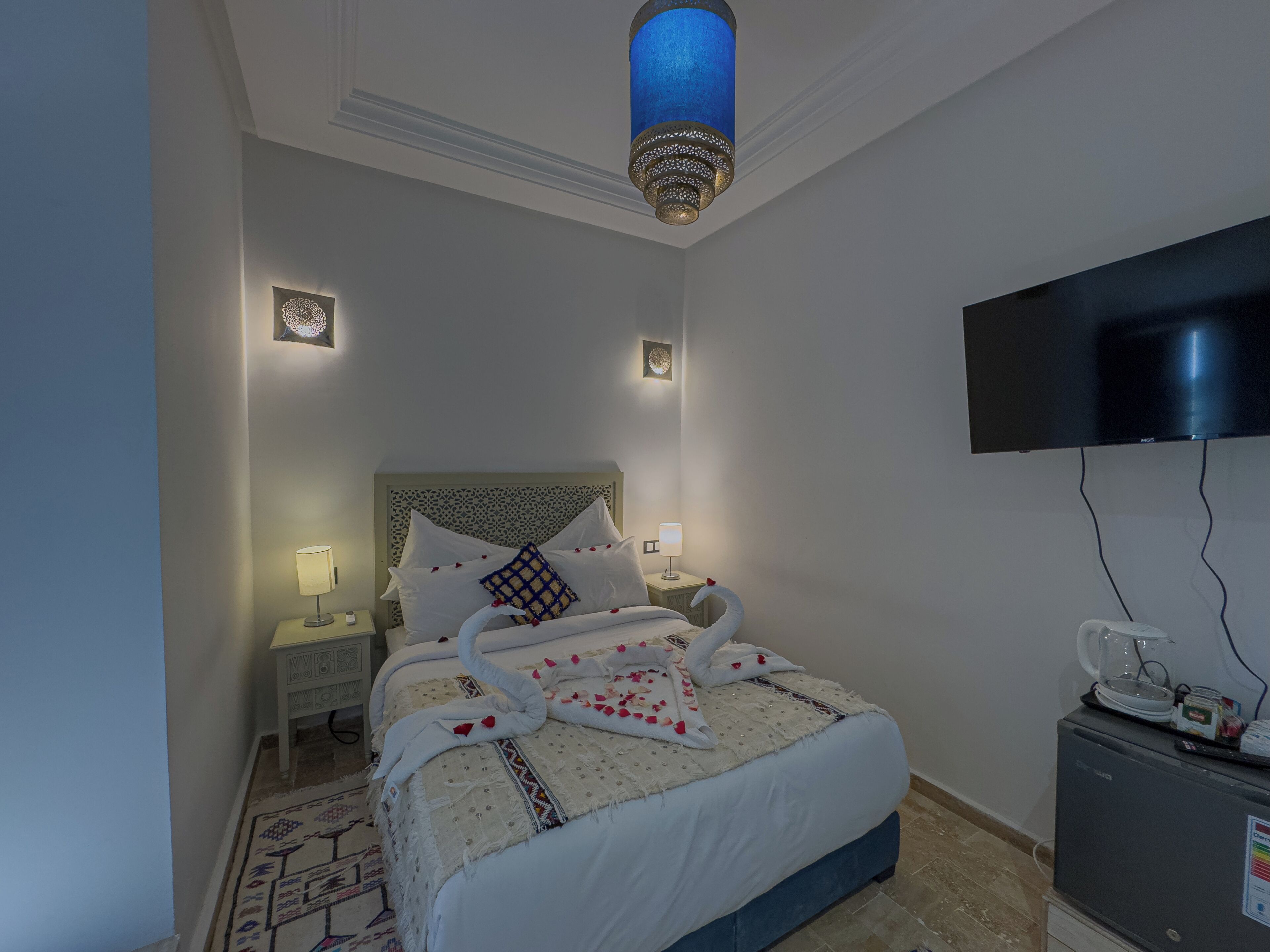 A neatly arranged bedroom with a bed, bedside lamps, a television, and a minibar.