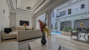 A spacious living area with a sofa, a dining table, and a TV mounted on the wall. - Riad Tonaroz Gold (Marrakech)