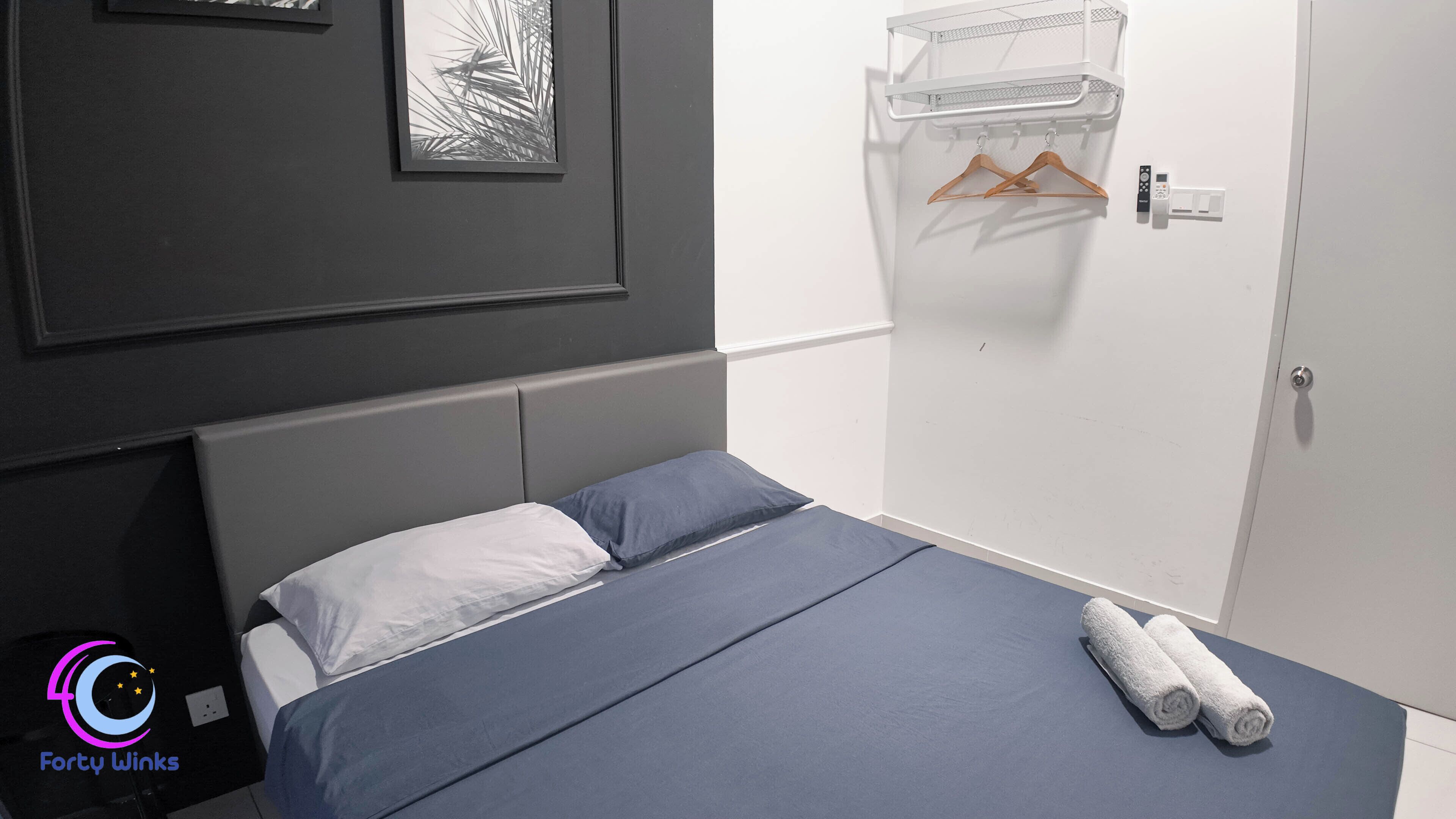 A bedroom with a bed, a wall-mounted shelf with hangers, and a door with a control panel.