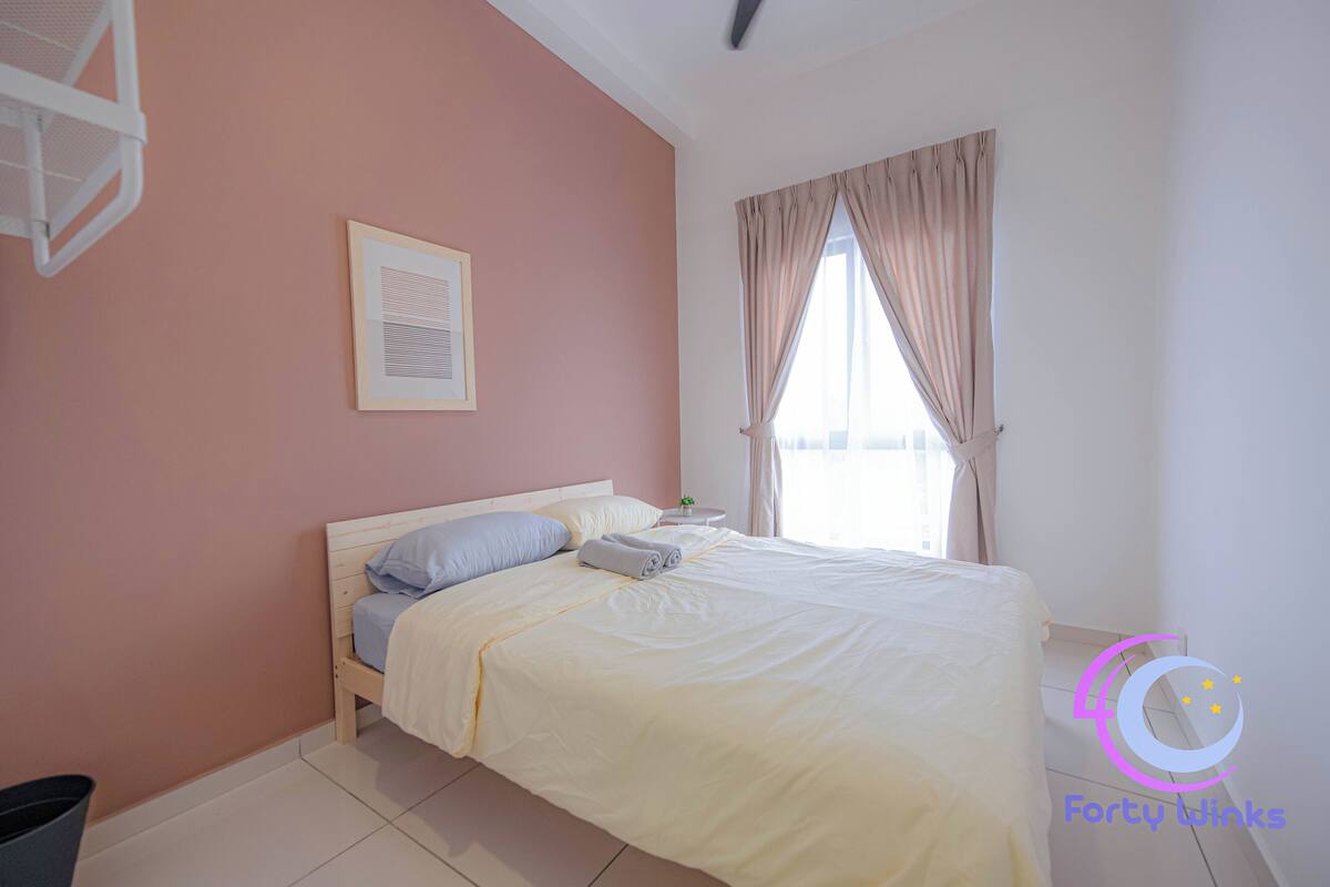 A bedroom with a bed, a framed picture on the wall, a window with curtains, and a small table with a plant.