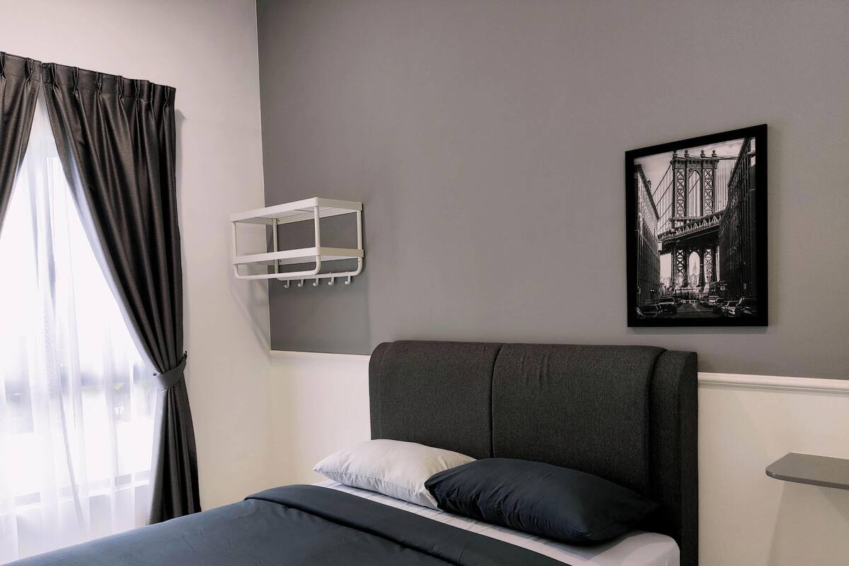 A modern bedroom with a large bed, a headboard, a window with curtains, a wall-mounted shelf, and a framed picture.