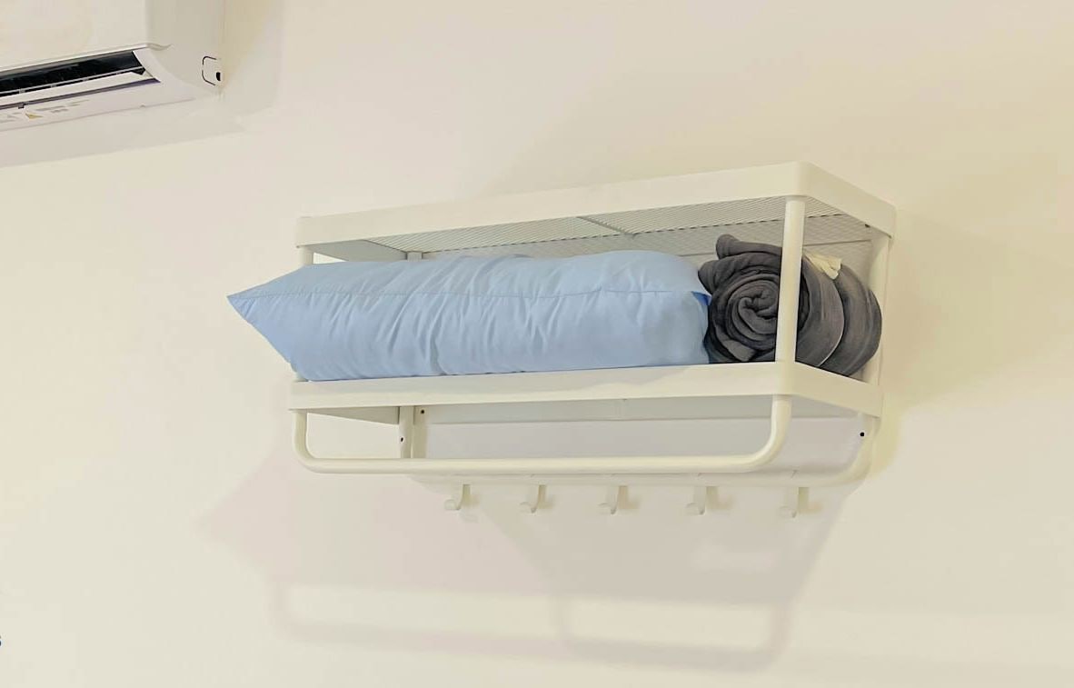 A white bedside unit with a blue pillow and rolled-up blanket.