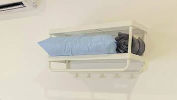 A white bedside unit with a blue pillow and rolled-up blanket.
