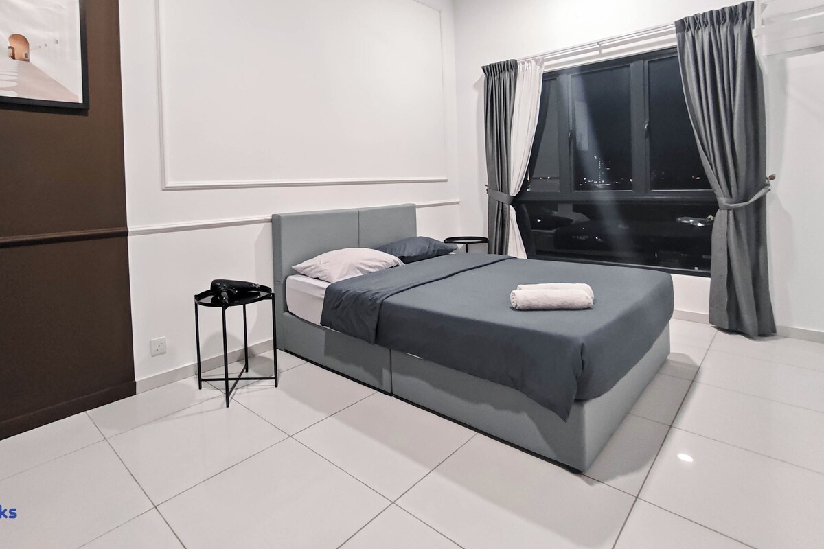 Un dormitorio moderno con cama, mesita de noche, ventilador de techo, ventana con cortinas y vista a la ciudad.