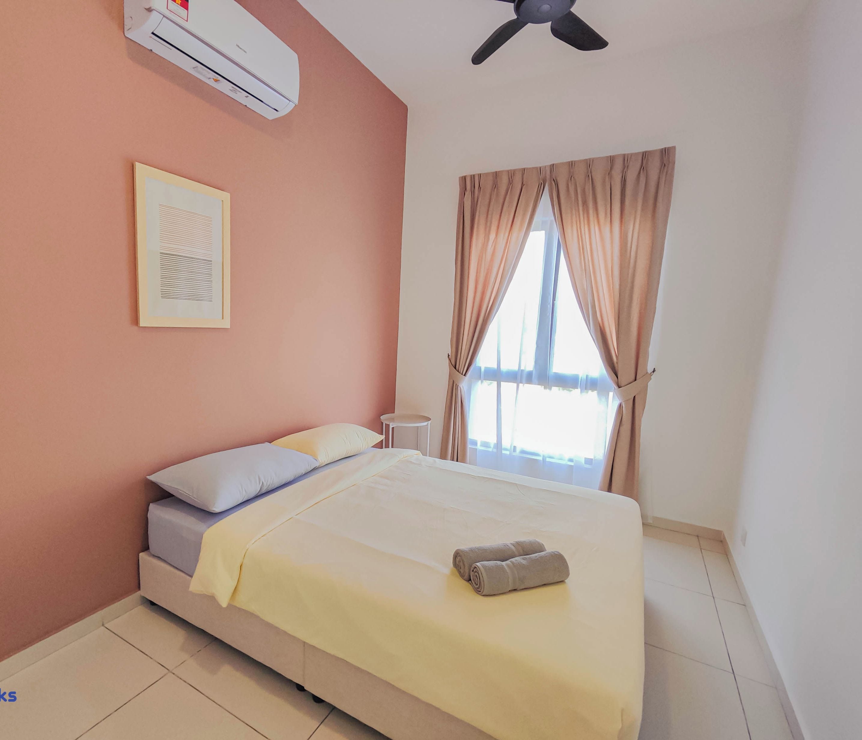 A bedroom with a bed, an air conditioning unit, a ceiling fan, a window with curtains, and a small bedside table.