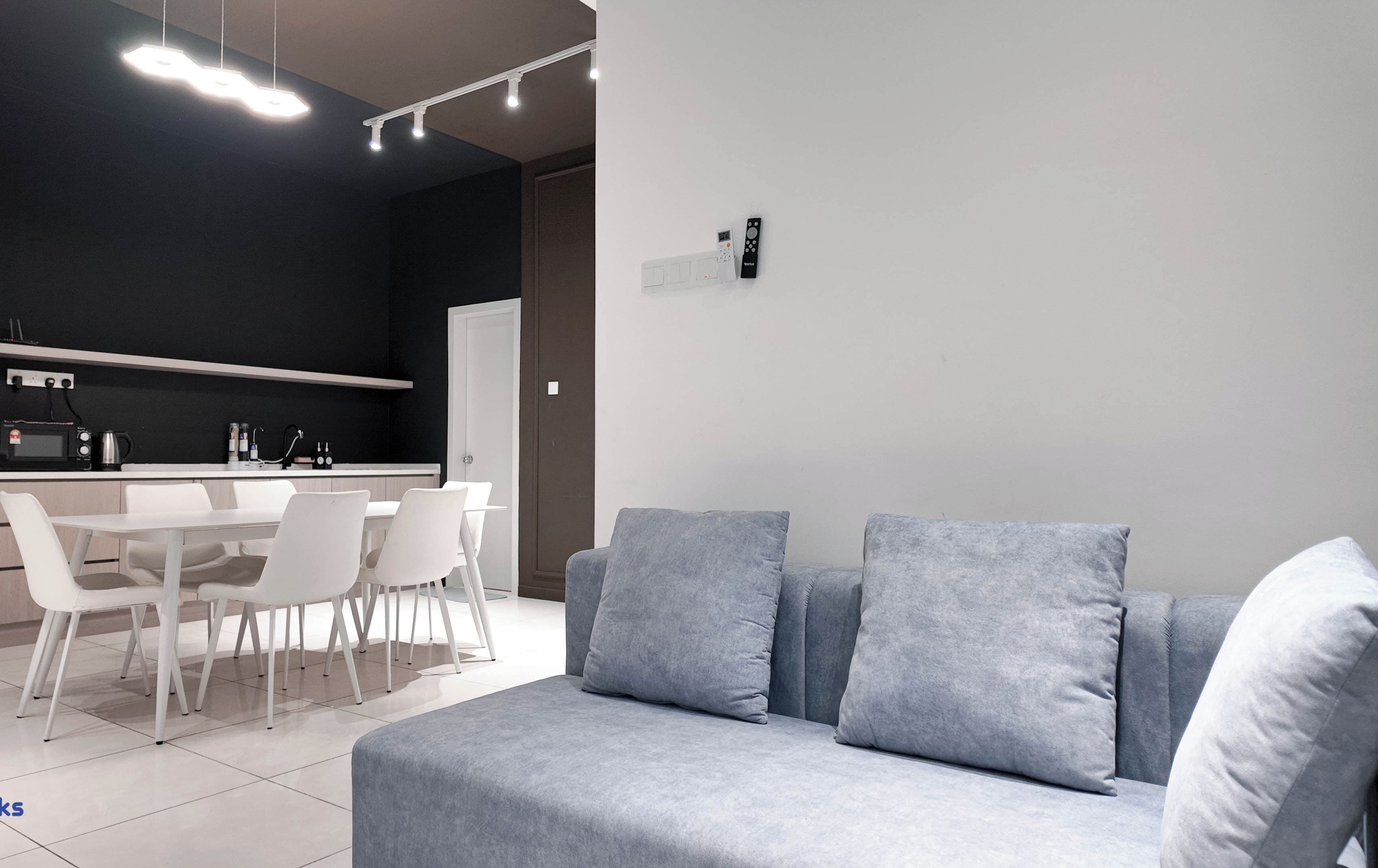 A modern kitchen with white appliances, a dining area with a white table and chairs, and a grey sofa with cushions.