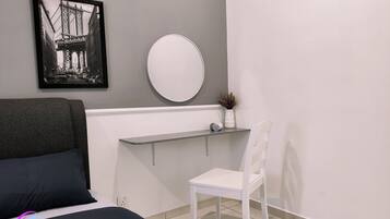 A bedroom with a bed, a desk, a chair, a mirror, and a framed picture on the wall.
