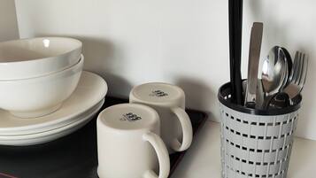 A set of white bowls and mugs on a tray, with a utensil holder containing spoons and forks.