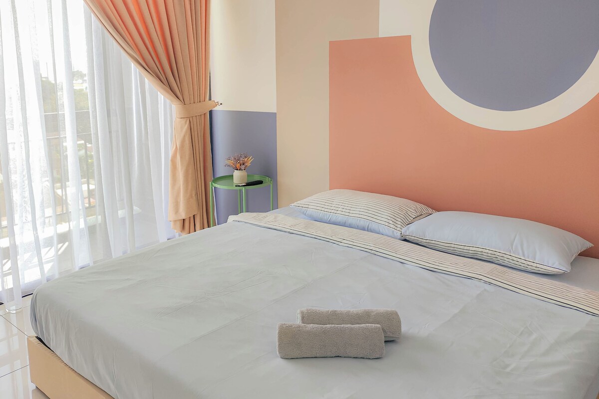 Habitación de hotel con cama, almohadas, una mesita de noche con un jarrón y vistas al exterior.