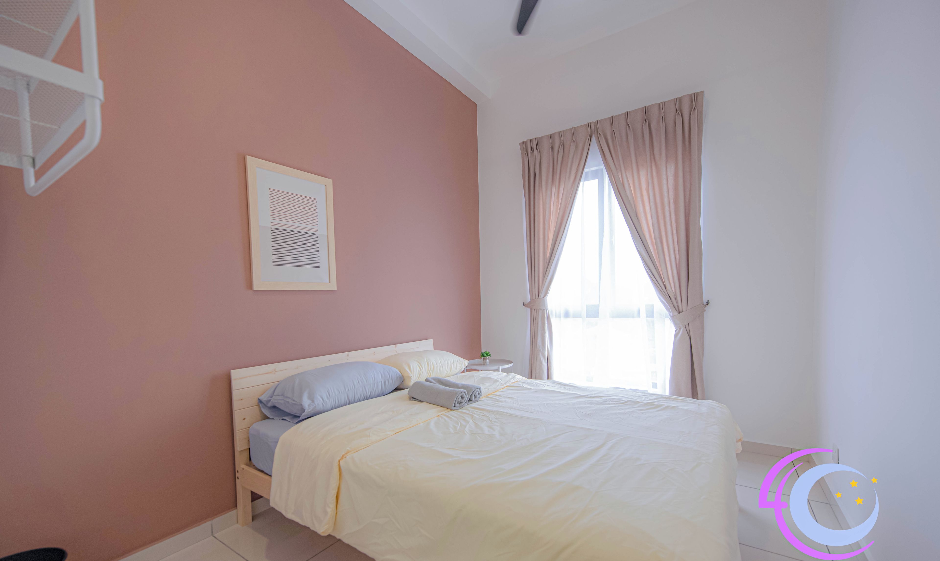 A bedroom with a bed, a framed picture on the wall, a window with curtains, and a small table with a plant.