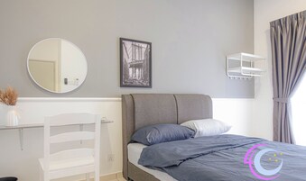 A modern bedroom with a grey bed, white chair, and a framed picture on the wall.