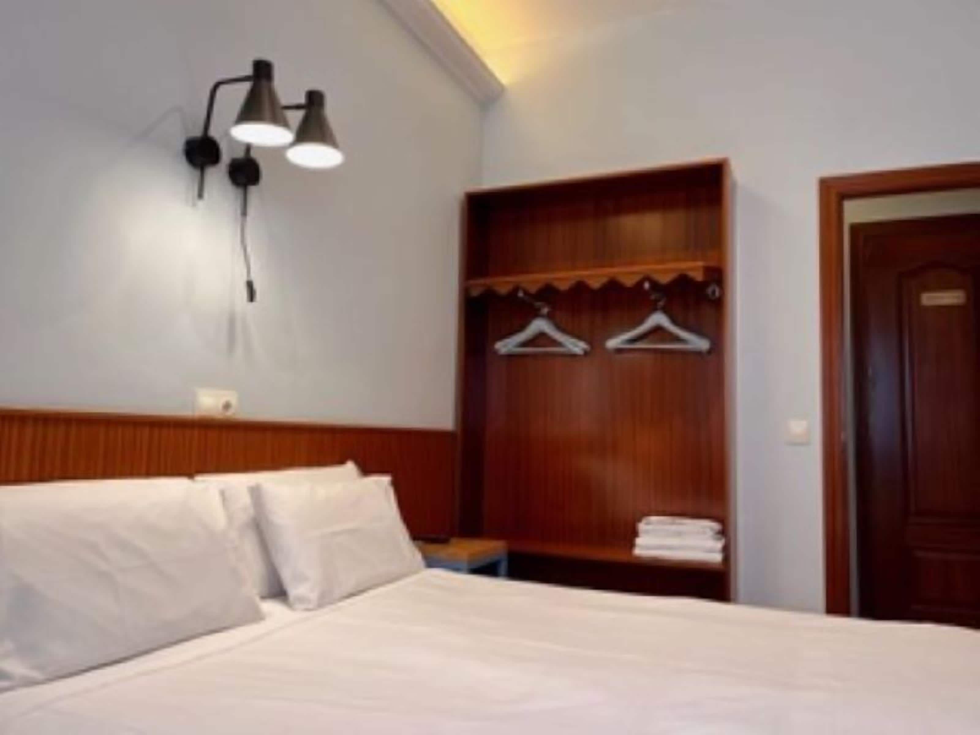 Un dormitorio con cama, un armario de madera y una lámpara fijada a la pared.