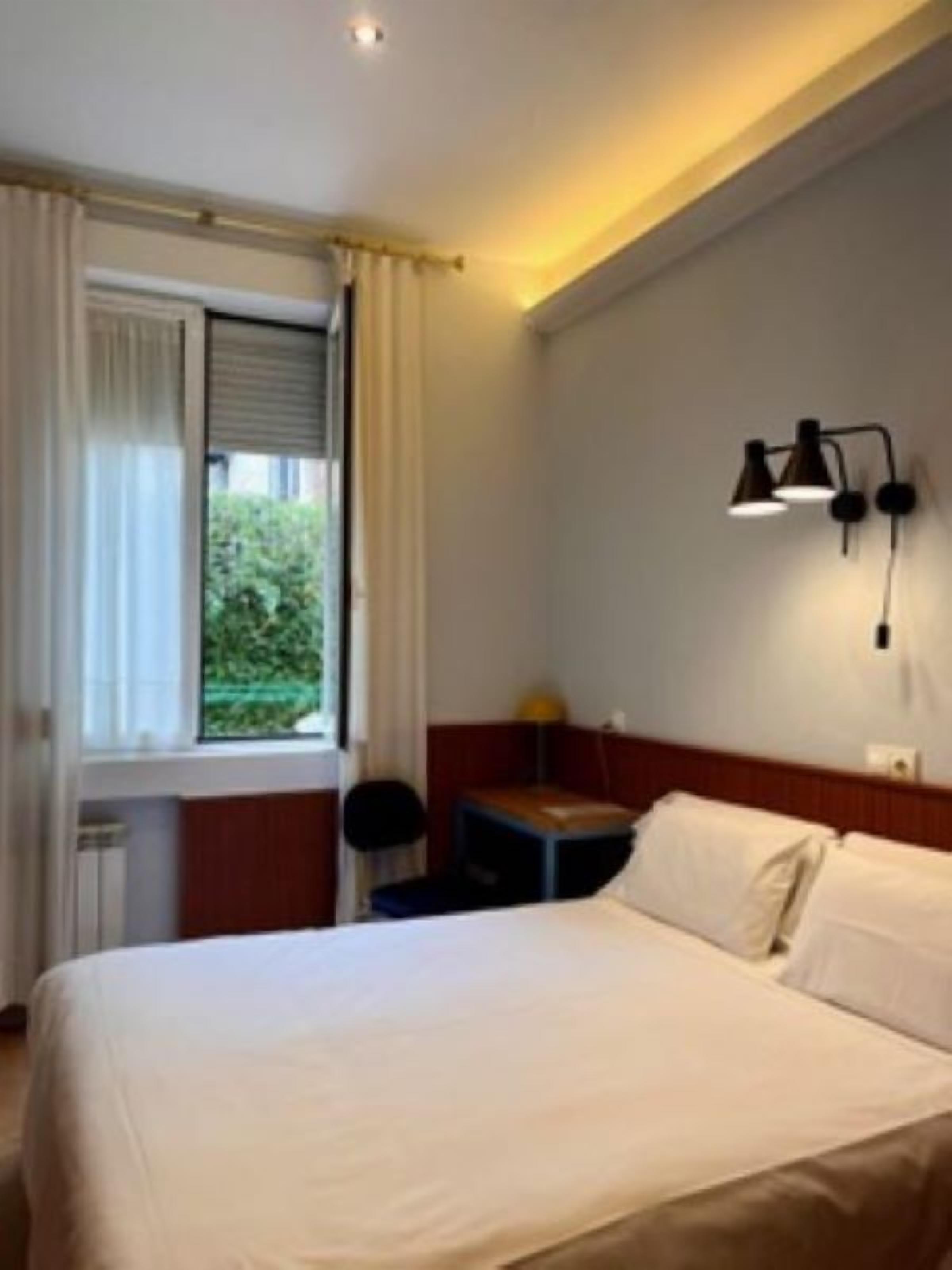Une chambre d’hôtel avec un lit, une table de chevet, une lampe et une fenêtre avec des rideaux.