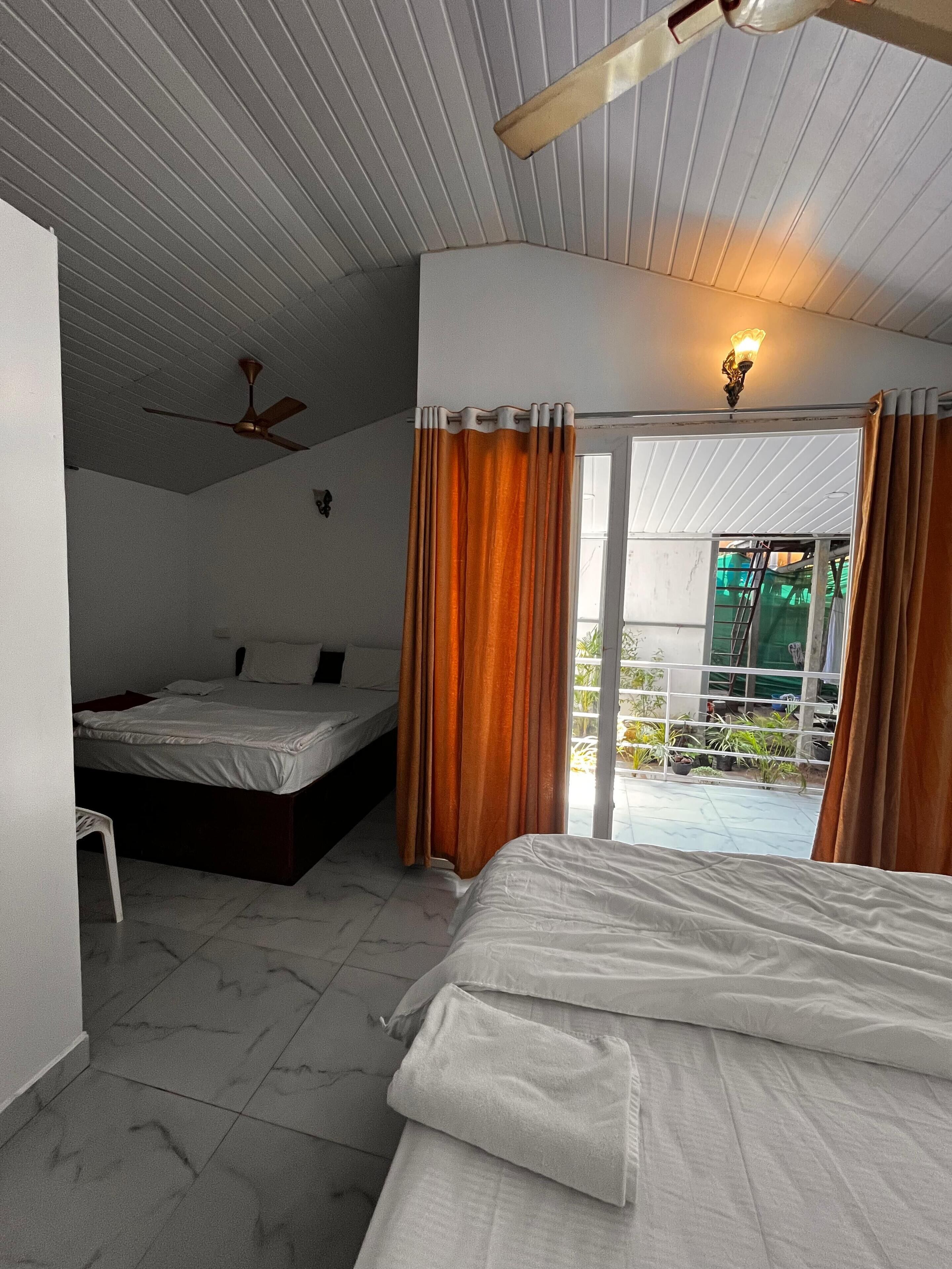 A bedroom with two beds, a ceiling fan, and a view of the outside balcony.