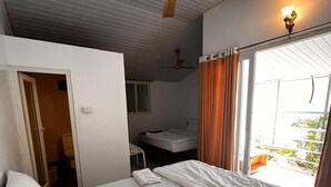 A hotel room with a bed, a ceiling fan, a window with curtains, and a view of the outside. - Casa Fiesta (Canacona)