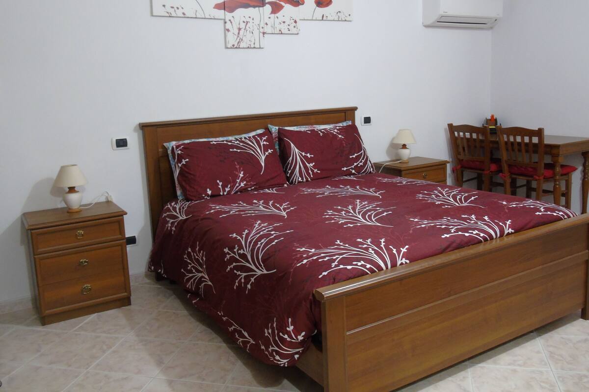 Een slaapkamer met een houten bed, een nachtkastje, een stoel en een klein tafeltje.