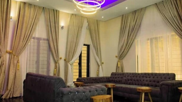 A room with a sectional sofa, two wooden side tables, and a modern chandelier. - 6BDR Duplex in GRA Near Shoprite & Malls (Enugu)
