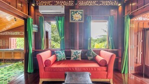 A wooden interior with a red sofa, green curtains, and a view of greenery outside. - 6BR Villa Huge Pool & Mountain View V89 (Rawai)