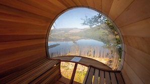 Una estructura de madera circular con un banco y una mesa, que ofrece vistas a un lago y al paisaje circundante.