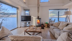 Una sala de estar moderna con un ventanal grande con vistas a un lago, una chimenea, un televisor y una zona de estar acogedora.