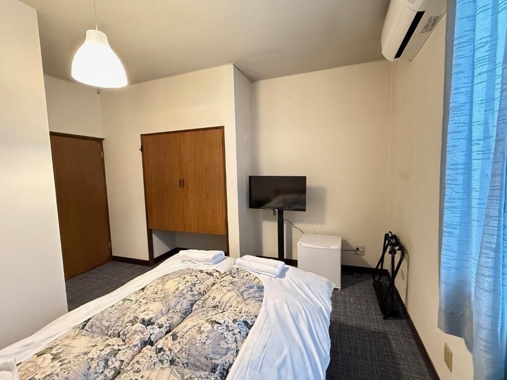 A hotel room with a bed, a television, a wardrobe, and a window with curtains.