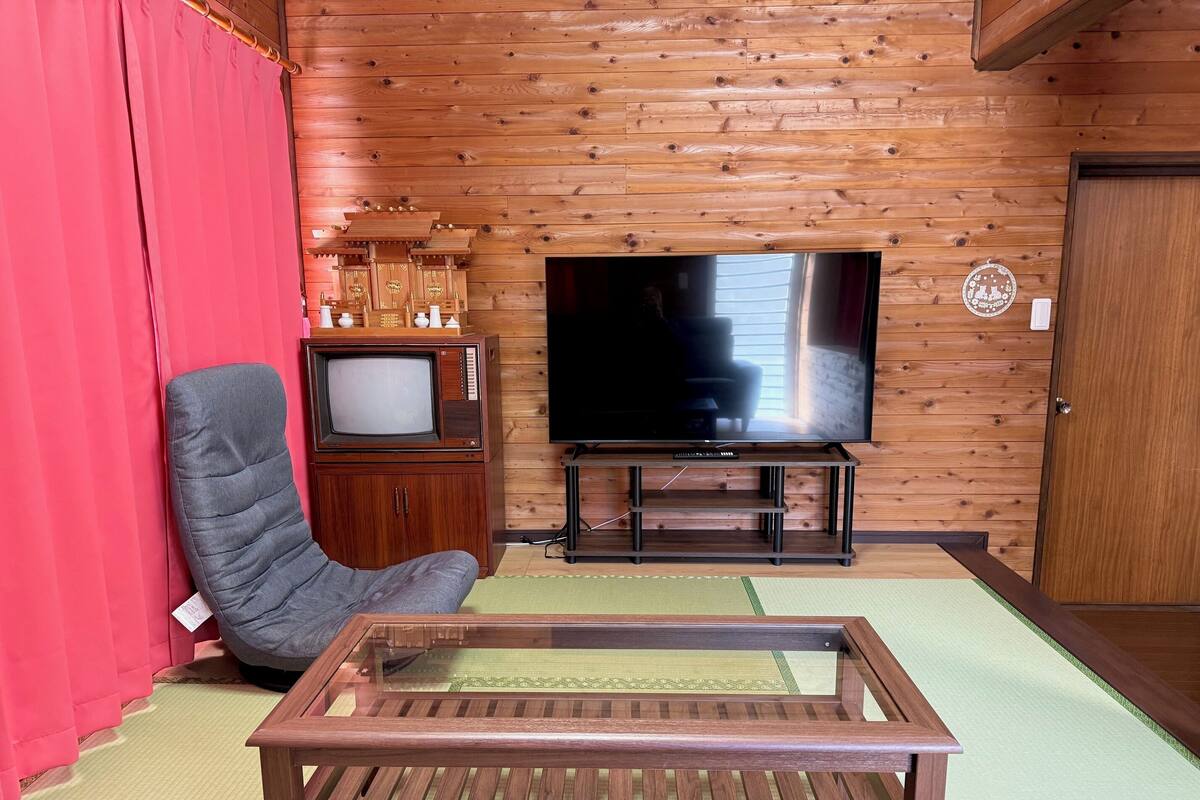 A room with a wooden wall, a television, a wooden cabinet, a chair, and a table.