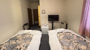 Une chambre d’hôtel avec deux lits, une télévision, un appareil de climatisation et une petite table avec une tasse.